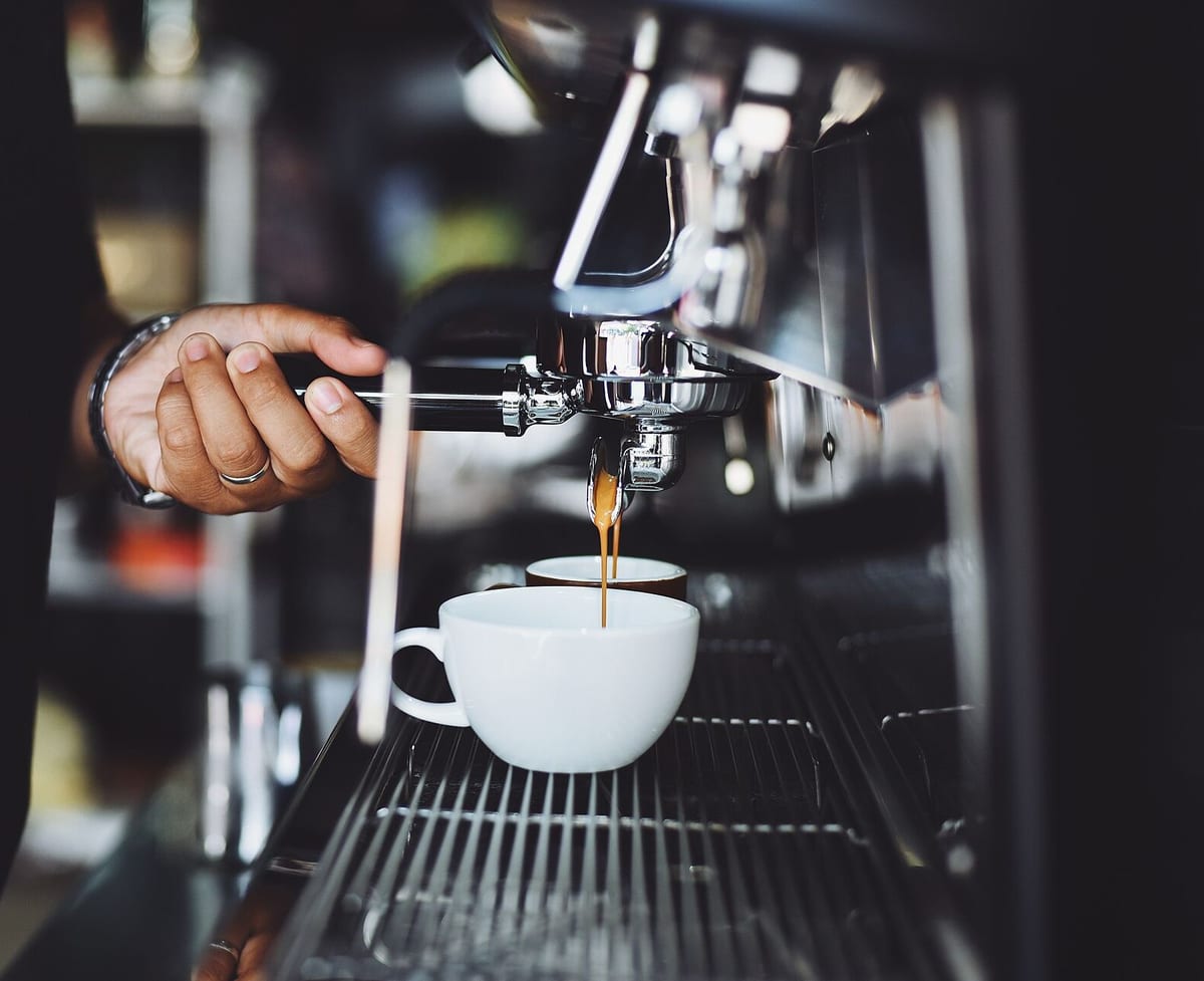 Hand på filterhållaren till en espressomaskin medan kaffet rinner ner i en vit kopp