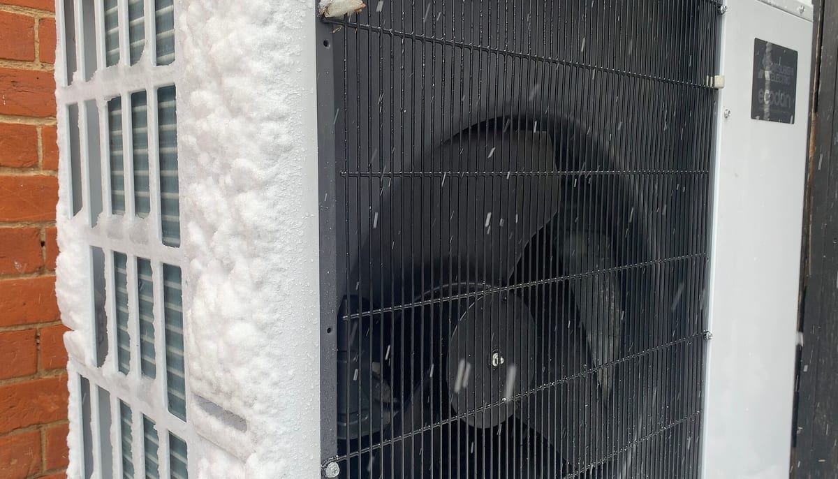 Utomhusdelen av en värmepump monterad mot en husvägg, med snö på och runt höljet